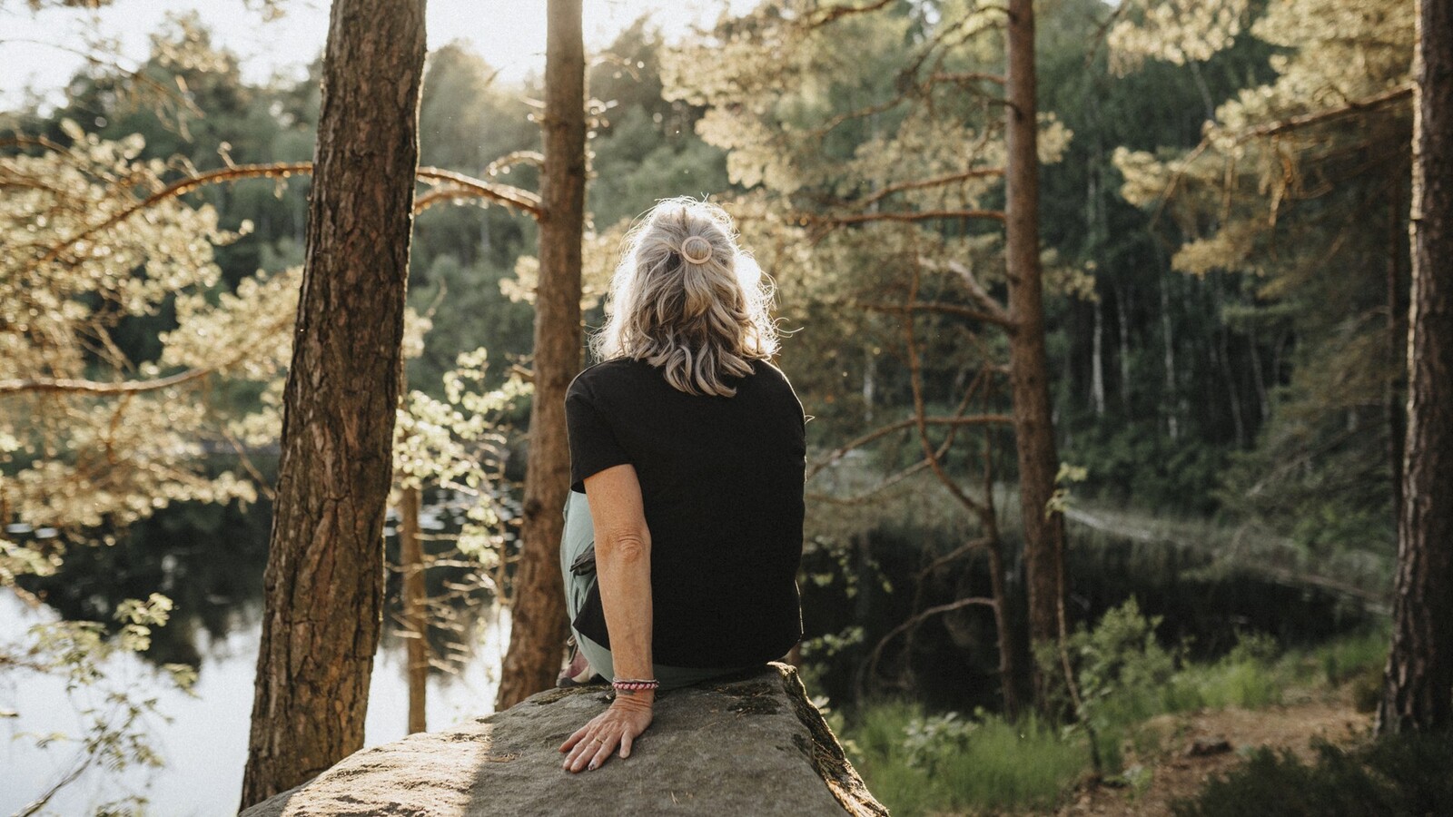 woman sits on a stone in the forest by water