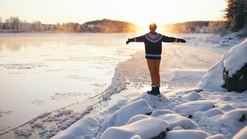  Person with outstretched arms on snowy rock by river.