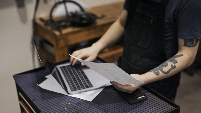 person med tatuering vid laptop i verkstad 