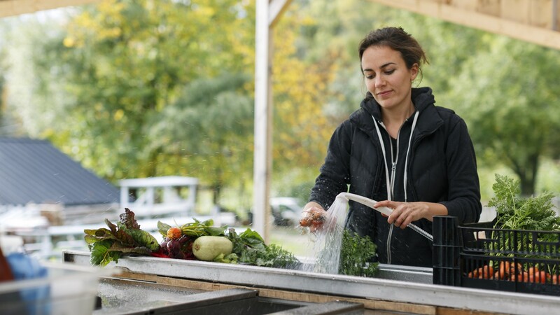 woman rinses vegetables in an outdoor kitchen