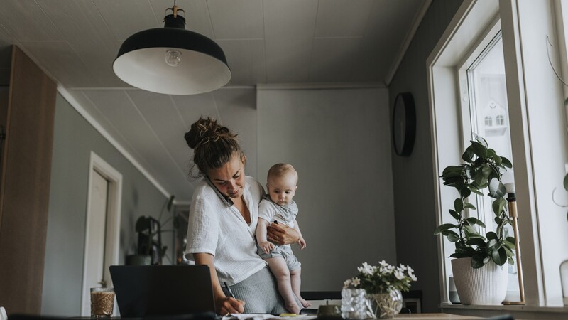 mamma med litet barn i famnen skriver och pratar i mobil