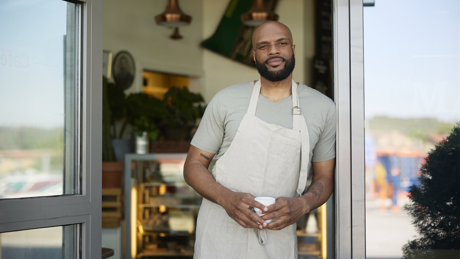 A man leans against the door frame with a cup of coffee in his hand
